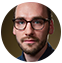 Person with glasses and facial hair against a dark background, looking at the camera.